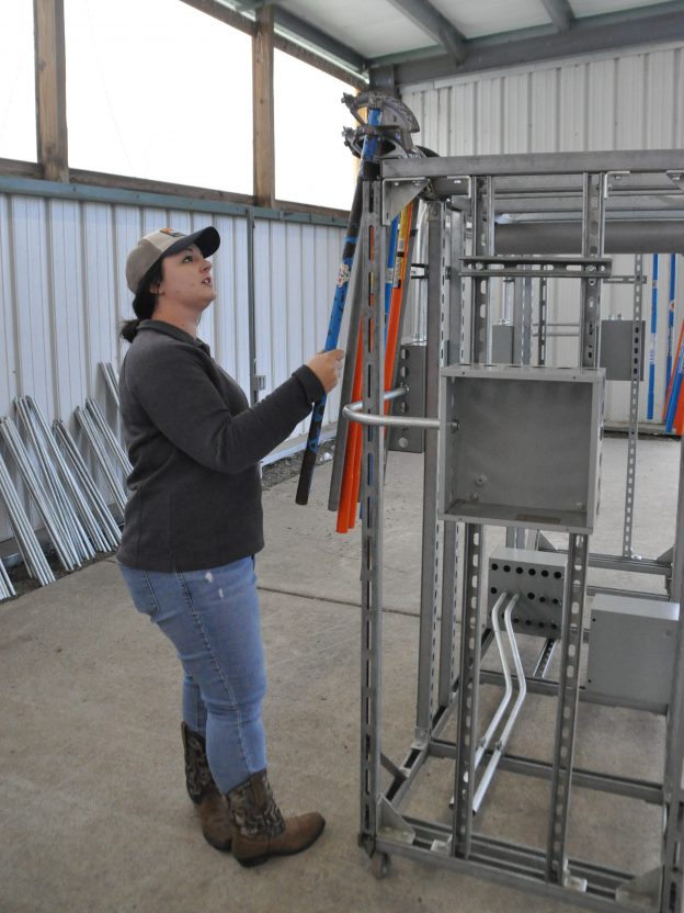 Erin Pope hangs conduit tools on a rack.