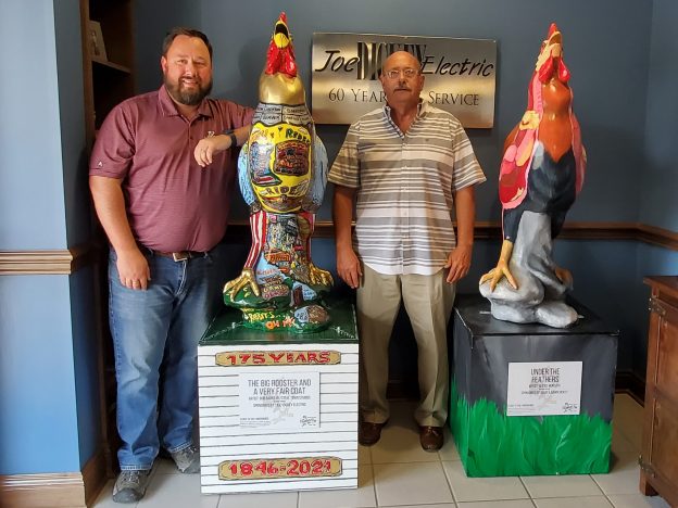 Eric Carlson and Dave Dickey of "Joe" Dickey Electric stand with rooster statues decorated by local artists.