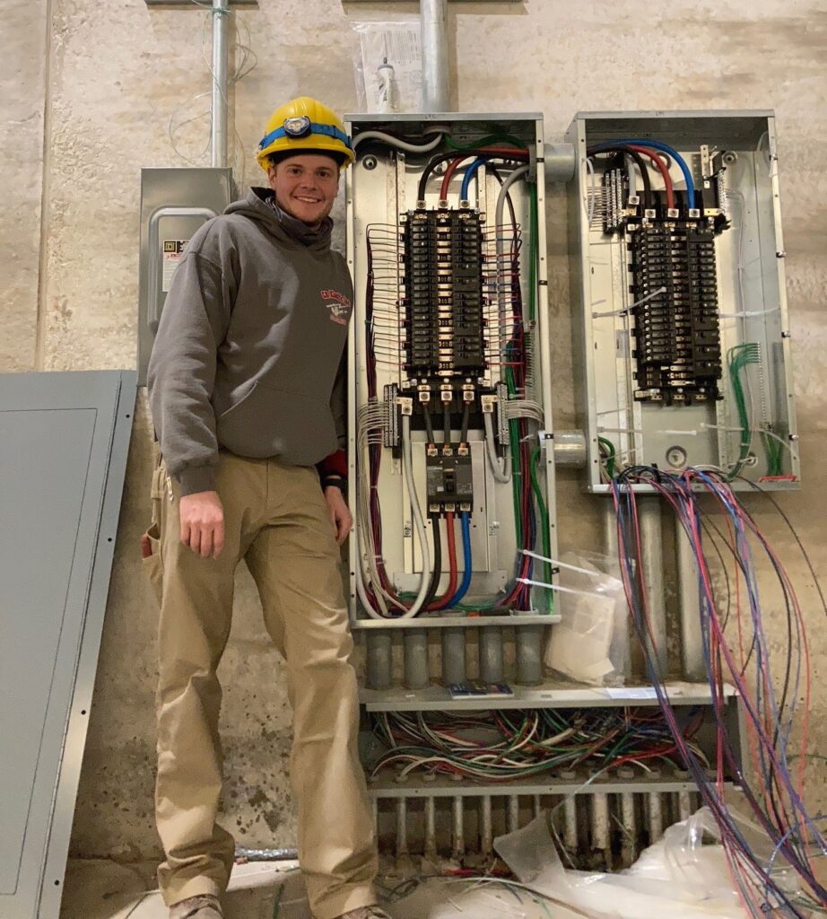 Luke Gale, a commercial/industrial apprentice, working near a large electrical panel in the field.