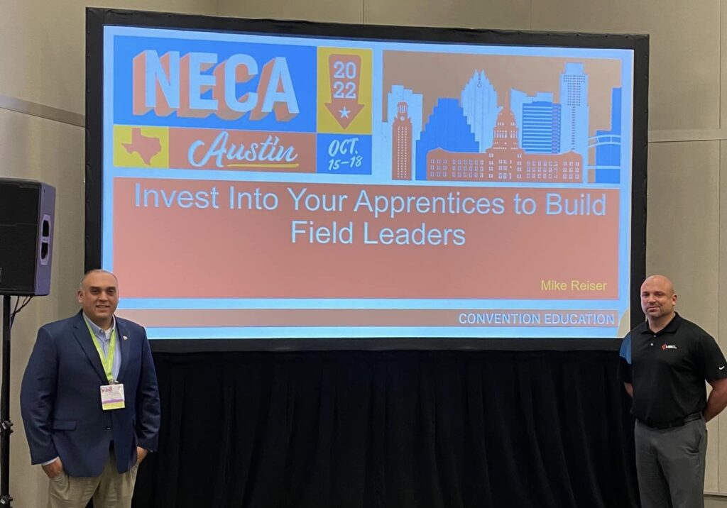 Bruno Frate and Michael Reiser pose in front of their presentation's title page at the 2022 NECA Convention in Austin, Texas. 