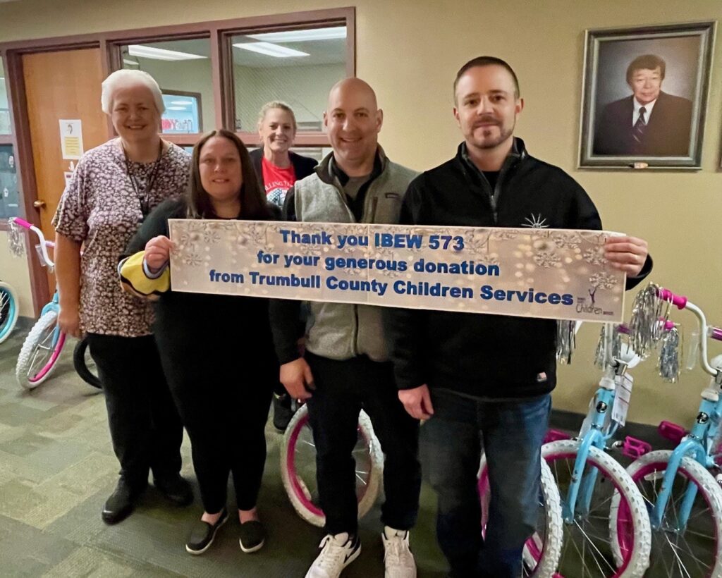 Todd Ambrose, IBEW Local 573 business manager, Mark Phillips, IBEW Local 573 president/organizer, with Trumbull County Children Services employees accepting bike donation with "thank you" banner.