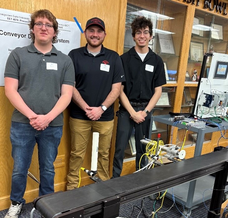 Nick Waldon (left), Alex Birtalan, and Brad Zouck (right), at YSU's STEM Showcase with their senior project, a conveyor detection system.